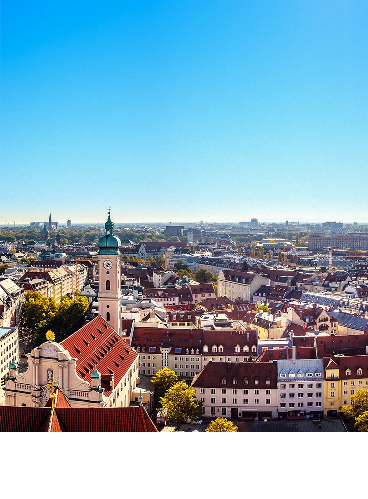 LOUIS Hotel Muenchen Viktualienmarkt Skyline Stadtansicht von München bei klarem Himmel, mit Kirchturm und bunten Gebäuden im Vordergrund.