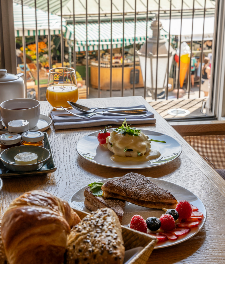 Breakfast table at the LOUIS Hotel with pastries, eggs, juice and a view of the lively Viktualienmarkt in Munich.