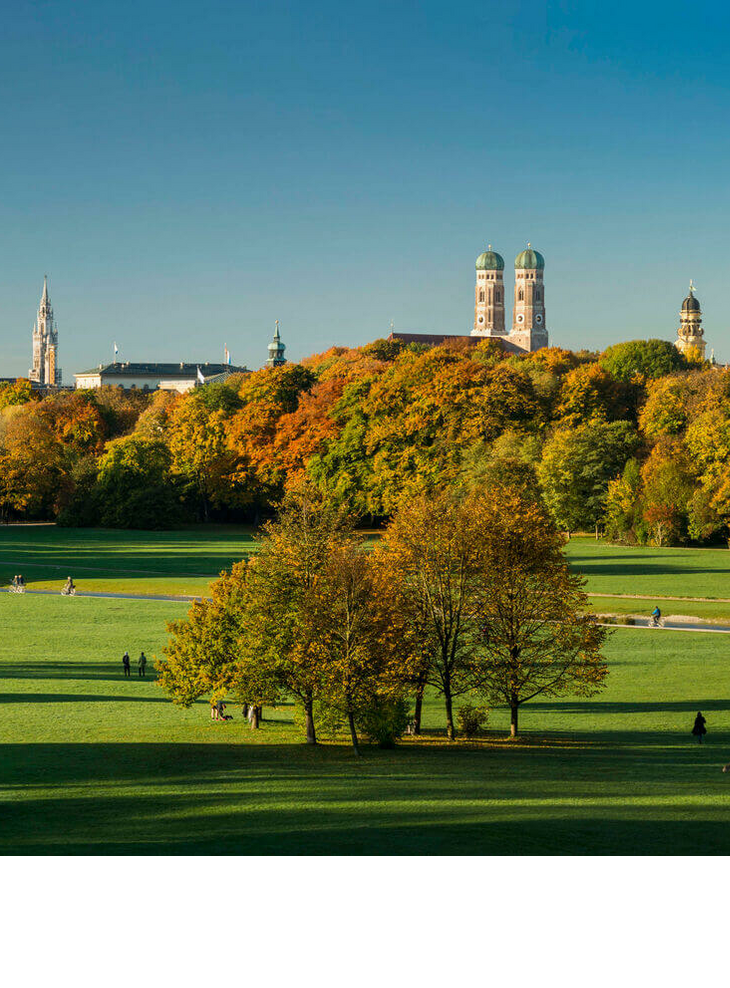 Panorama in the English Garden Spacious park with green meadows, colorful autumn trees and a city silhouette in the background under a clear sky.
