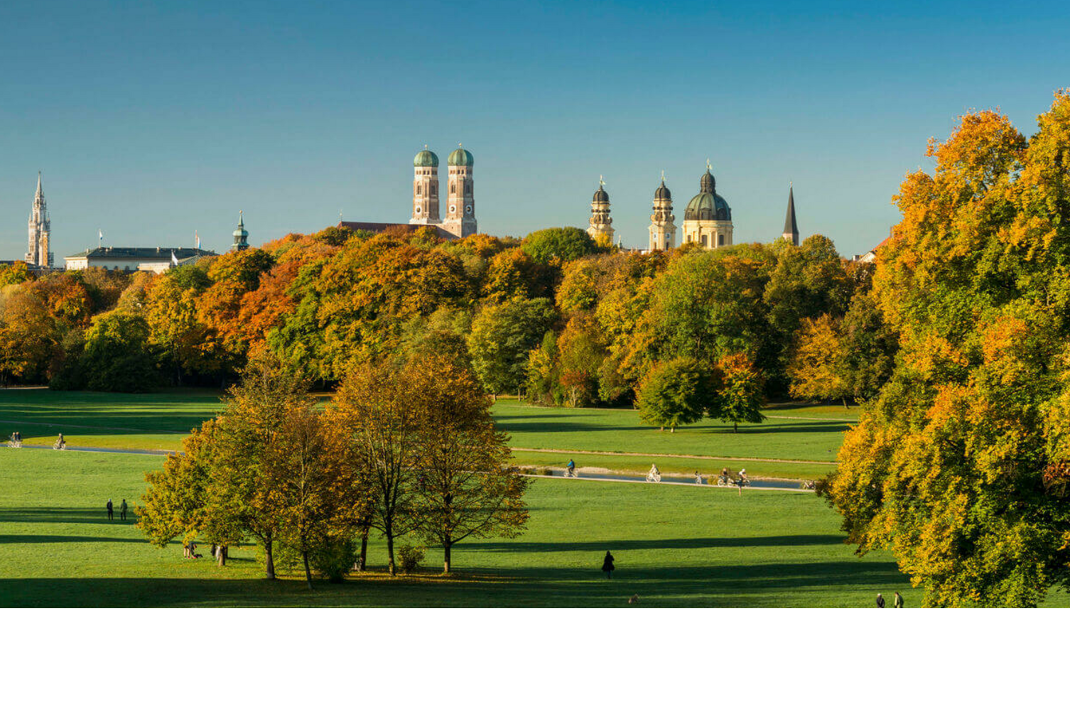 Panorama in the English Garden Spacious park with green meadows, colorful autumn trees and a city silhouette in the background under a clear sky.