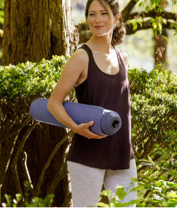 Frau mit Yogamatte neben einem Baum