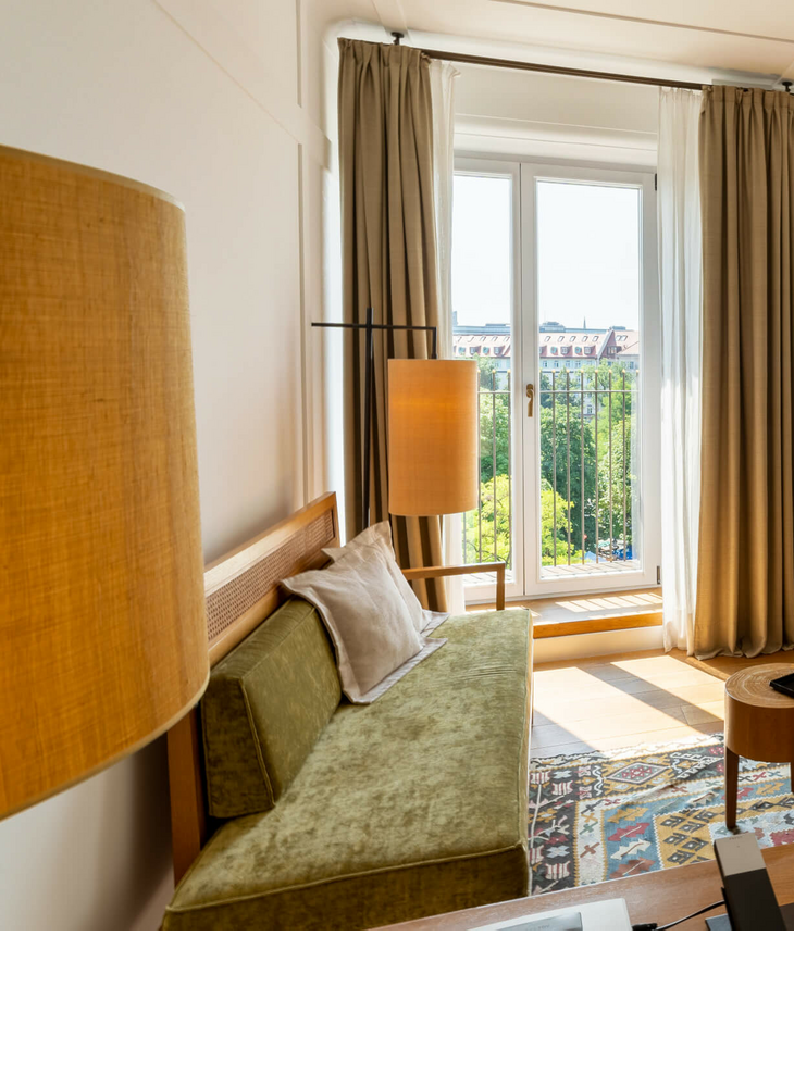 LOUIS Hotel München | Zimmer Market View Deluxe Helles Hotelzimmer mit modernen Möbeln, großen Fenstern und Blick auf die Stadt im LOUIS Hotel München.