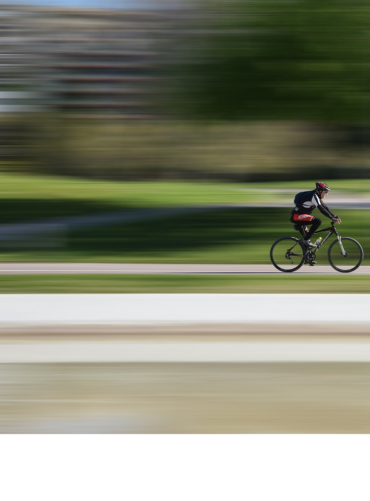 Race - Bicycle Cyclist wearing a red helmet riding fast on a cycle path through a green park.