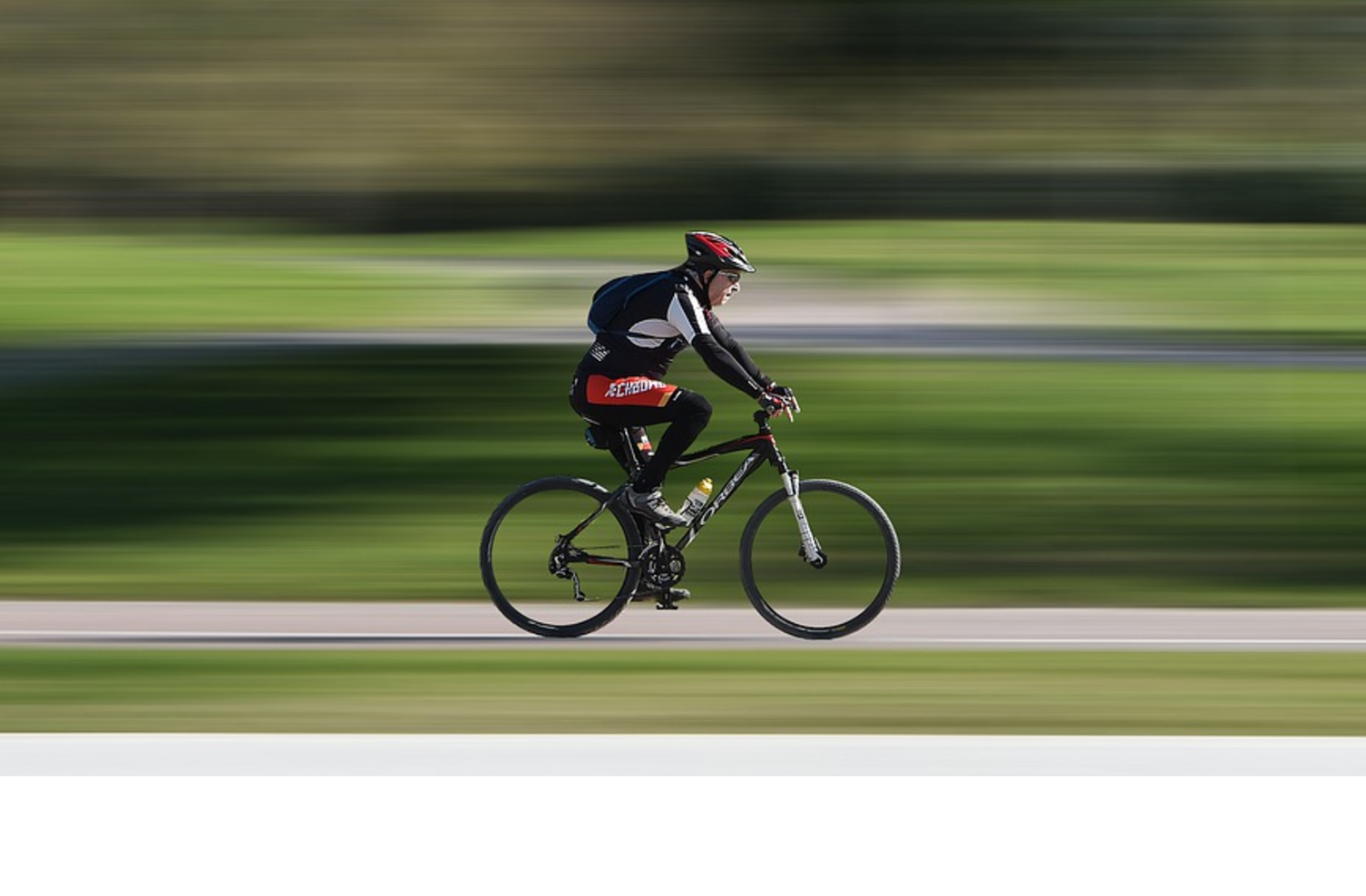 Race - Bicycle Cyclist wearing a red helmet riding fast on a cycle path through a green park.