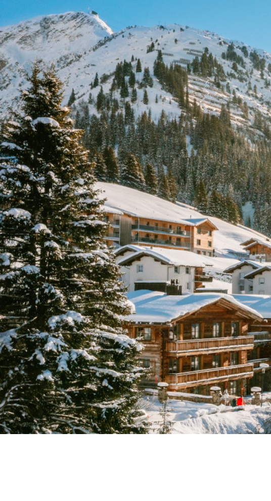 Skipanorama Lech am Arlberg – The Alpine Retreat Verschneite Alpenlandschaft mit Sonne über Hotel Severin*s in Lech, umgeben von Bergen und Bäumen.