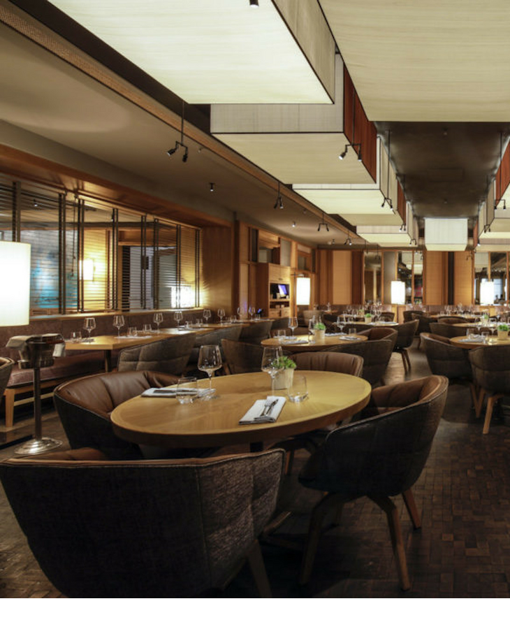 The LOUIS Grillroom at the Viktualienmarkt in Munich Elegant hotel restaurant with modern wooden furniture, laid tables and atmospheric lighting.