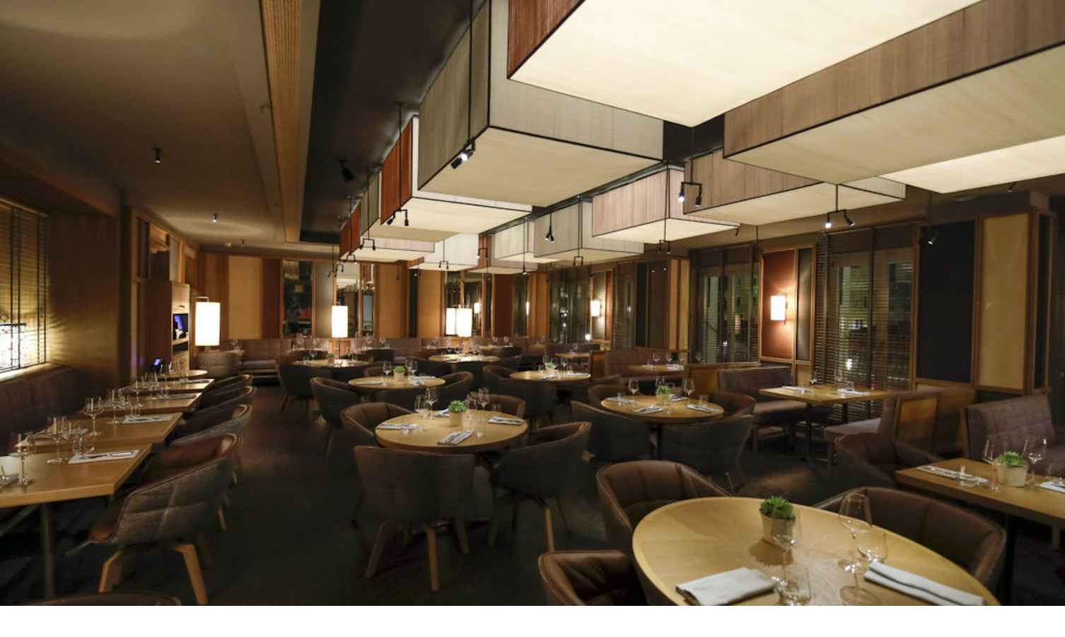 The LOUIS Grillroom at the Viktualienmarkt in Munich Elegant hotel restaurant with round wooden tables, comfortable chairs and atmospheric lighting.