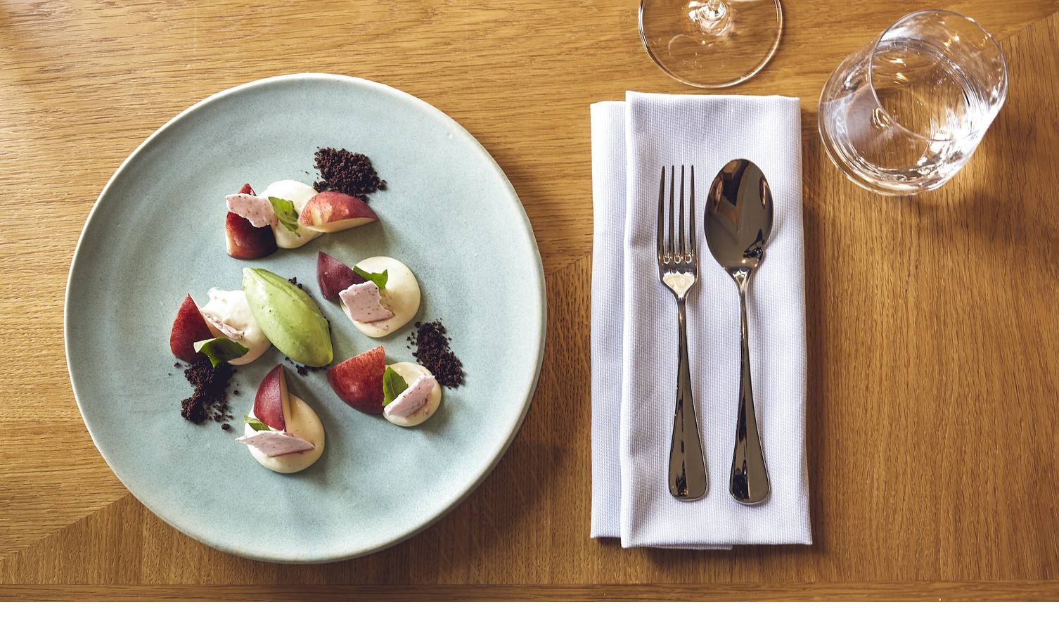 Grillroom Restaurant ice cream dessert LOUIS Hotel Munich Elegant dessert on a blue plate with cutlery and glasses on a wooden table in the LOUIS Hotel Munich.