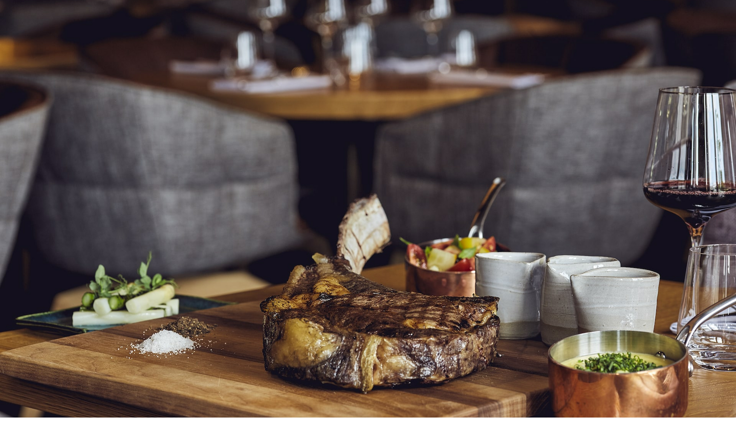 High-quality meat grilled to perfection at The LOUIS Grillroom in Munich Elegant steak dish with side dishes and a glass of red wine on a wooden table in the stylish restaurant of the LOUIS Hotel Munich.
